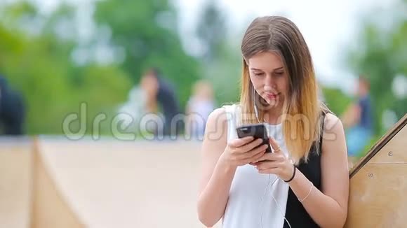 年轻的高加索女人在欧洲城市在户外发送信息和听音乐戴墨镜的漂亮女孩坐着视频的预览图