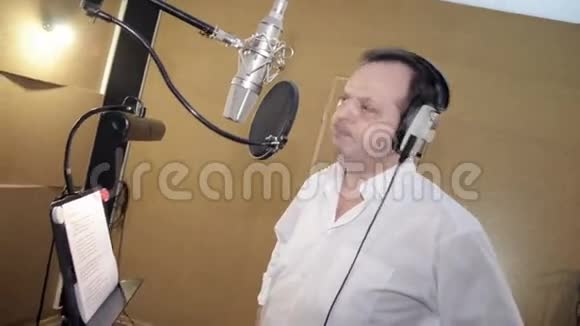 穿白色衬衫的人在麦克风前的耳机里唱歌摇滚工作室视频的预览图