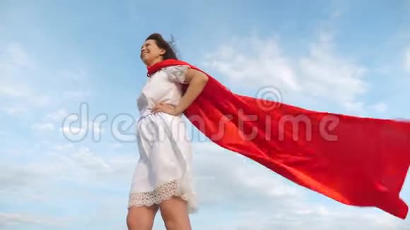 女孩梦想成为超级英雄性感的超级英雄女孩穿着红色斗篷站在田野上斗篷在飘舞视频的预览图