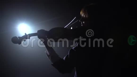 专业人士在一个黑暗的工作室里拉小提琴灯笼从它的眩光黑烟背景背面视频的预览图