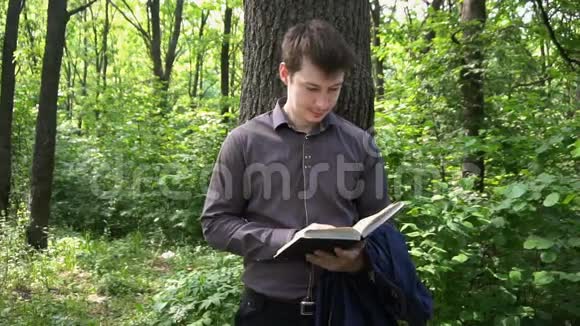 一个年轻的商人在树林里的一棵树旁看书视频的预览图
