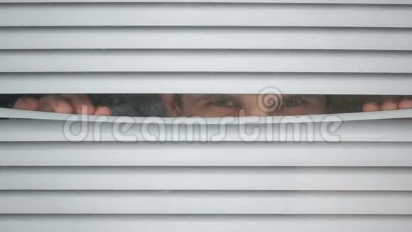 一个人透过百叶窗看着窗外的街道监视着嫌疑犯视频的预览图