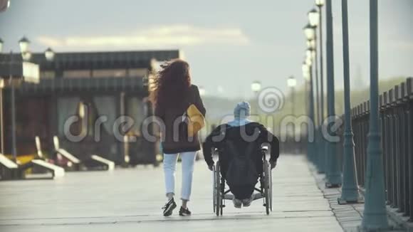 年轻快乐的女人和坐轮椅的残疾人一起在码头上散步视频的预览图