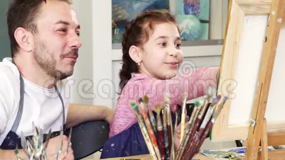 骄傲的父亲看着他可爱的女儿画一幅画视频的预览图
