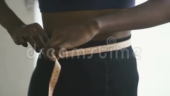 在家穿运动服装的年轻黑人妇女的特写镜头美国黑人女孩用黄色胶带测量腰部视频的预览图