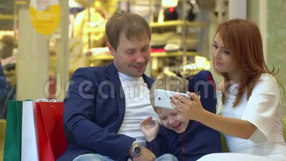 圣诞节可爱的夫妇和孩子在购物中心慢镜头一对夫妇坐在购物中心的沙发上视频的预览图