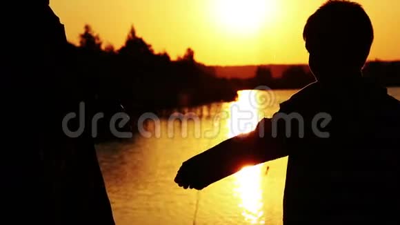 日落时分母亲抱着儿子在河边夕阳余晖映在水面上视频的预览图