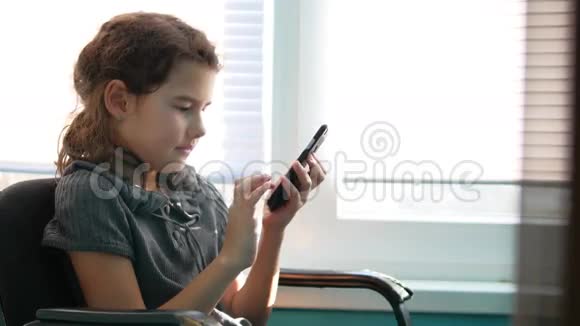十几岁的女孩坐在窗边玩智能手机玩网络游戏视频的预览图