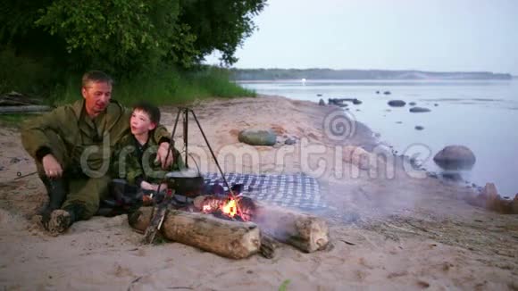 父子俩围坐在湖边的篝火旁视频的预览图