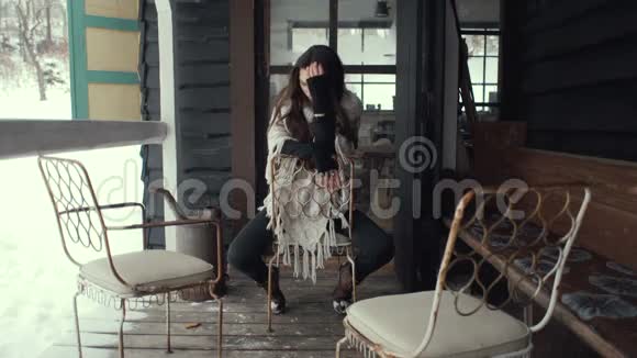 美丽的黑发女人穿着针织毛衣坐在房子旁边视频的预览图