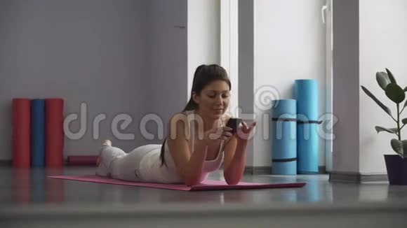 女孩躺在瑜伽垫上看着电话视频的预览图