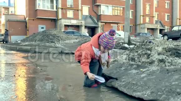 穿着橡胶靴的女孩在靠近纸船的水坑上跳跃视频的预览图