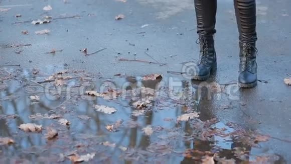 穿着黑色战靴的女孩在雨后的水坑里飞溅视频的预览图