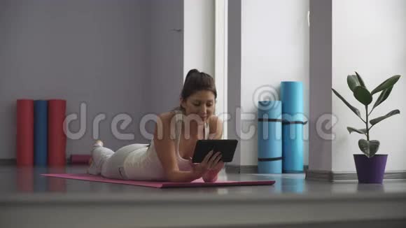 女人躺在瑜伽垫上看着平板电脑视频的预览图