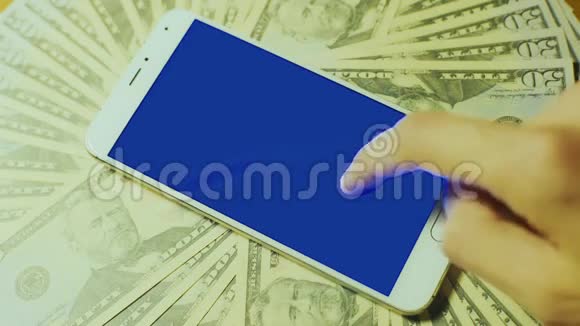 男性手触摸白色智能手机用蓝色钥匙显示在一堆钱上视频的预览图