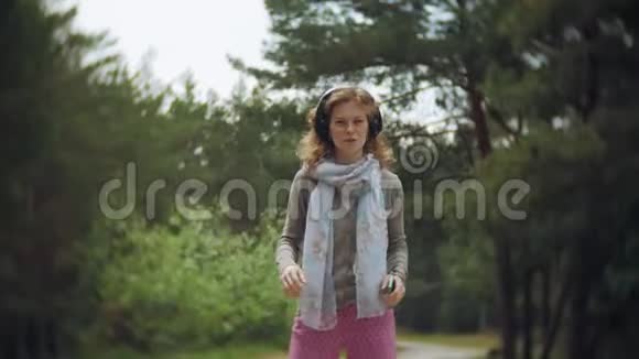 一个女人用耳机听音乐在一个美丽的绿色公园的岩石上放松一个常年年轻的女人视频的预览图