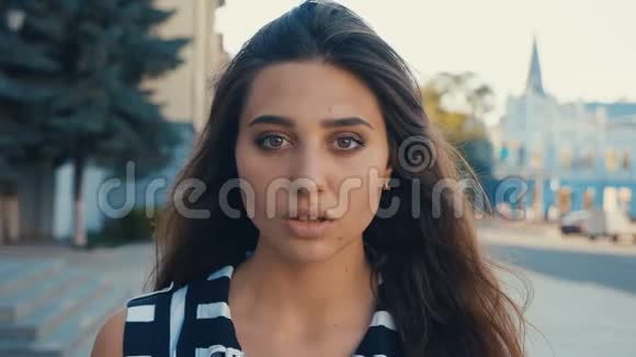 一幅美丽的年轻女子黑发模特的特写肖像在城市街道背景上看着相机女孩视频的预览图