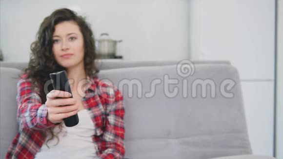 一个漂亮的女人看电视坐在沙发上手里拿着遥控器视频的预览图