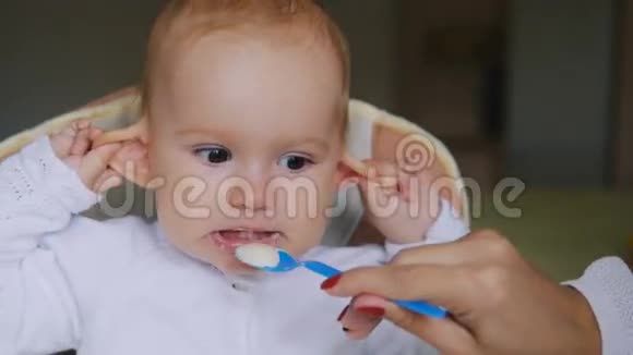 小女孩在儿童座椅上吃酸奶微笑幸福的家庭观念妈妈用勺子和婴儿食品视频的预览图