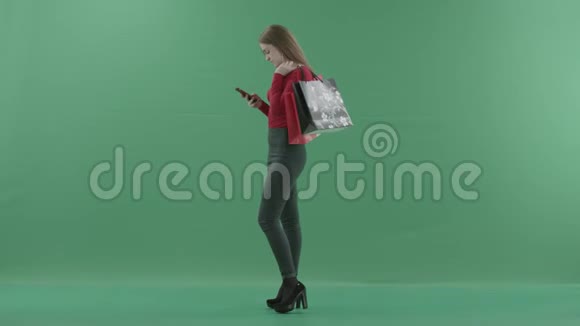 穿着便服的漂亮女人拿着购物袋在手机上发短信或上网视频的预览图