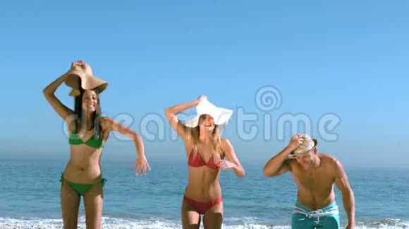 有魅力的朋友在海滩上跳着举起帽子视频的预览图
