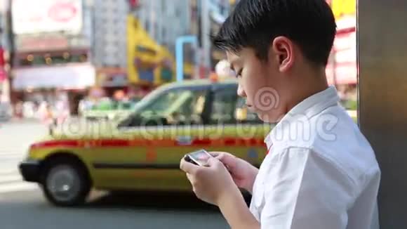 在日本东京步行街附近使用智能手机的快乐亚洲男孩视频的预览图