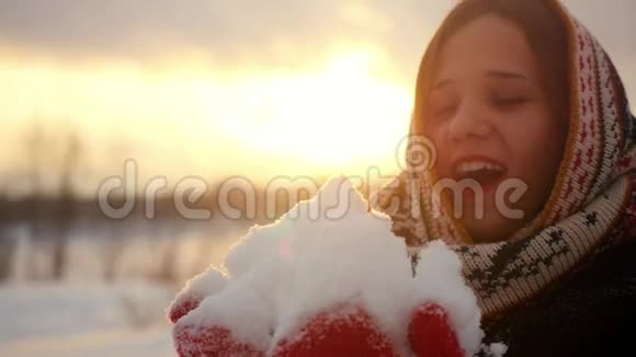一位美丽的年轻女子在日落时分用镜头轻轻地吹着雪花微笑着视频的预览图