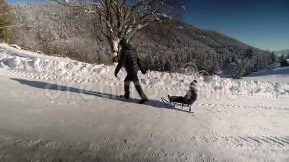 年轻的幸福家庭在雪林里玩得很开心父亲把他的小儿子卷在雪橇上爸爸和他的小儿子视频的预览图
