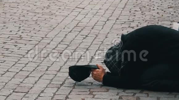 可怜的人用伸出的手和黑帽跪在人行道上期待着从路人那里捐赠硬币视频的预览图