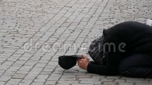 可怜的人用伸出的手和黑帽跪在人行道上期待着从路人那里捐赠硬币视频的预览图