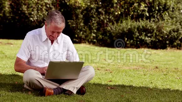 成熟的男人用笔记本电脑坐在草地上视频的预览图