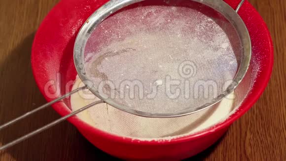 女人用筛子把面粉筛到木桌上的塑料碗里特写视频的预览图