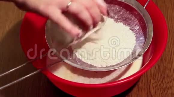 女人用筛子把面粉筛到木桌上的塑料碗里特写视频的预览图