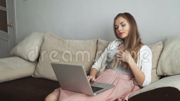 年轻女子坐在沙发上用笔记本电脑和微笑视频的预览图