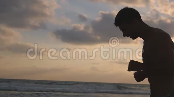 日落时分一个运动的年轻人在海边奔跑日出时运动员沿着海岸慢跑男性视频的预览图