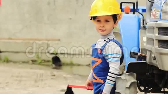 可爱的男孩就像工人站在拖拉机旁边视频的预览图