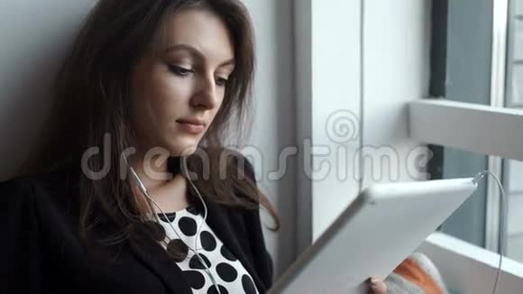 一位年轻女士在咖啡店用带耳机的平板电脑视频的预览图