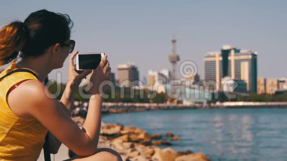 年轻女性使用移动电话坐在海边的堤岸和梅格波利斯摩天大楼上视频的预览图
