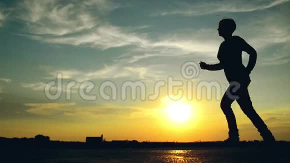 日落时分女人在街上奔跑一个女人在美丽的夏日天空中的剪影视频的预览图
