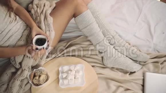 女人穿着温暖的毛衣躺在床上手里拿着一杯咖啡圣诞树新年的最高点拍摄视频的预览图