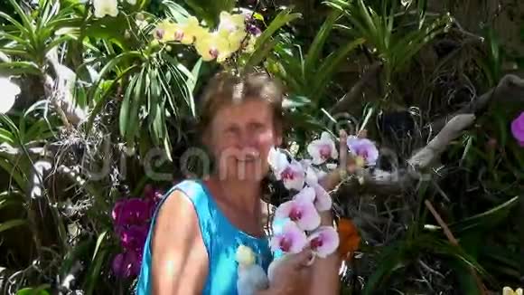 女人微笑着闻着欣赏着五颜六色的兰花视频的预览图