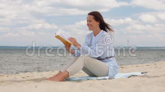 快乐微笑的女人在夏日海滩上看书视频的预览图