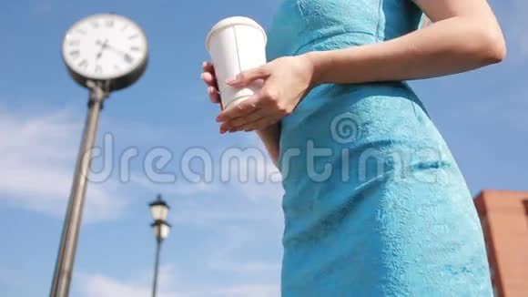 女孩站在时钟附近喝咖啡等待等待视频的预览图