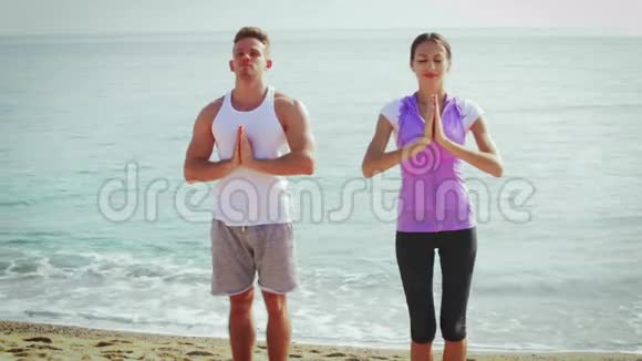 男人和女孩练习瑜伽姿势站在海滩上视频的预览图