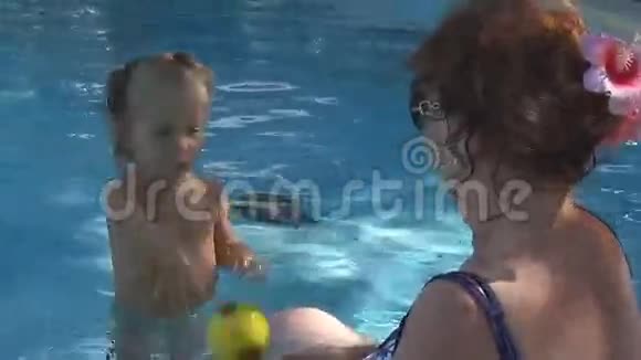 在游泳池里宝宝把一个黄色的球扔给漂亮的奶奶他们笑着玩视频的预览图