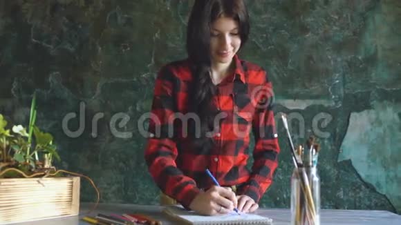 年轻的女艺术家用铅笔和微笑在纸笔记本上作画视频的预览图