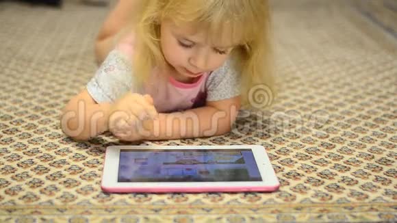 可爱的小女孩在平板电脑上工作躺在地毯上视频的预览图