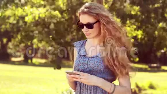 在公园里用手机高质量的4k格式金发美女视频的预览图