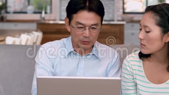 亚洲夫妇在沙发上用笔记本电脑视频的预览图