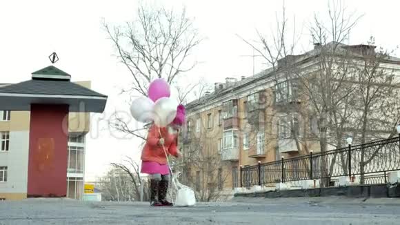 一个漂亮的小女孩在雨后的水坑上跳着五颜六色的气球视频的预览图